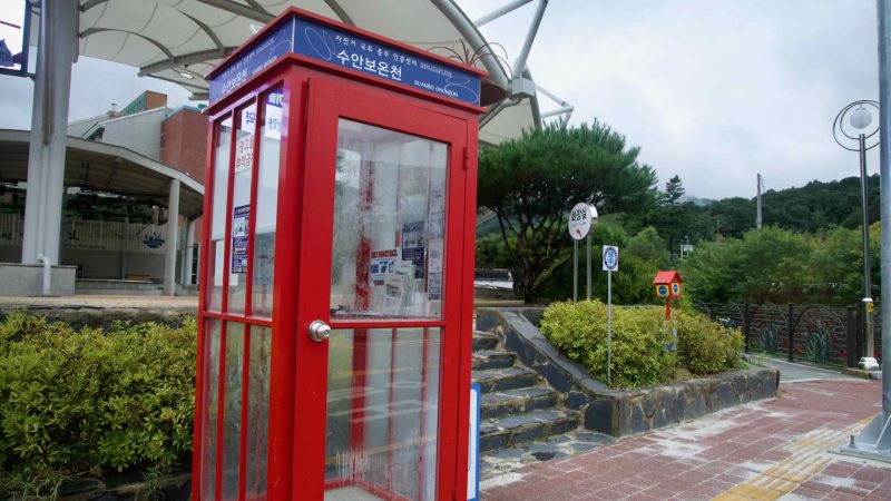 A red phone-booth style kiosk stands near the amphitheater at Multang Park.