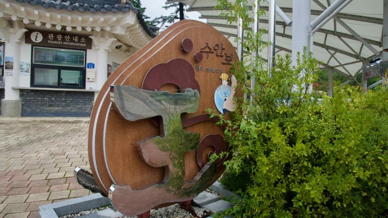 A tourist information booth and sculptural Suanbo sign sit under the park canopy.