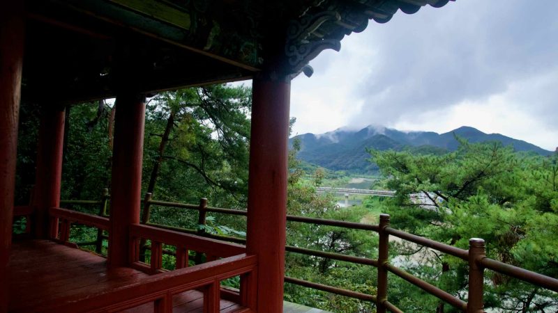 From the pavilion, pines and layered mountains lead to a river bridge near Sujupal Peaks.