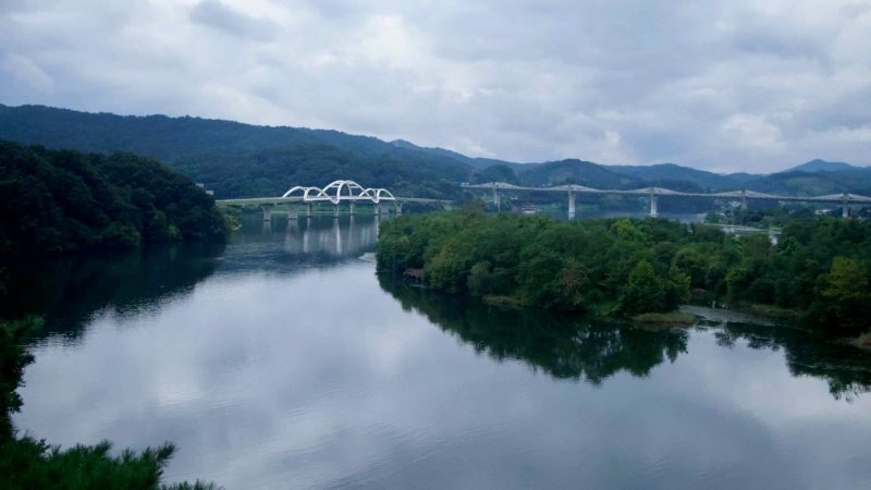 A graceful arched road bridge crosses the South Han River below Tangeumdae Park, its white spans mirrored on the water.