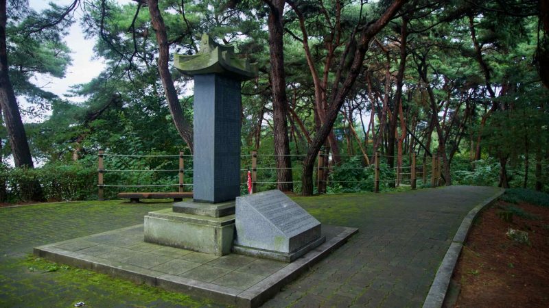 A stone stele and plaque stand beneath pines along a quiet walkway in Tangeumdae Park.