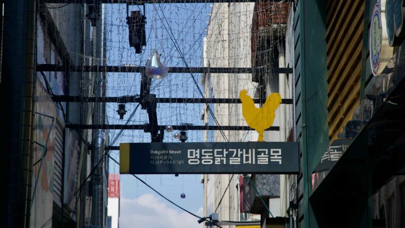 An overhead sign reading Dakgalbi Street with a yellow rooster icon hangs above the restaurant lane in Myeongdong.
