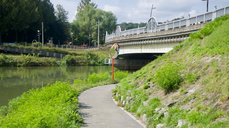 A riverside bike and walking path curves below a road bridge beside Gongji Stream, with green embankments and reflections on the water.