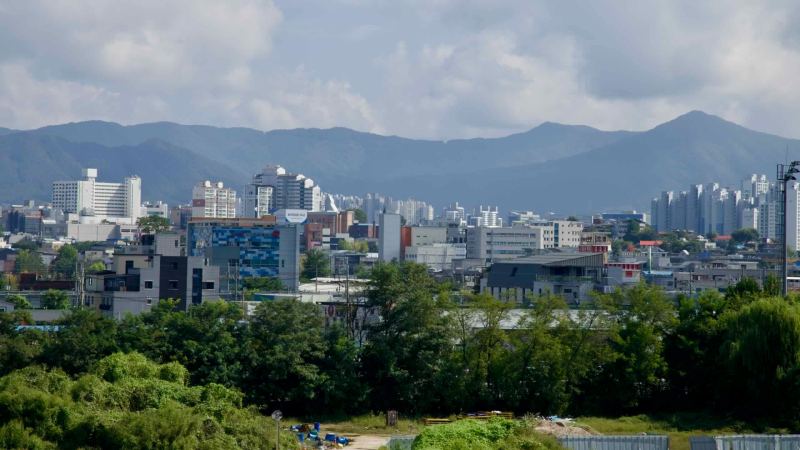Chuncheon’s downtown skyline rises against mountain backdrops with apartments, hotels, and clustered offices.