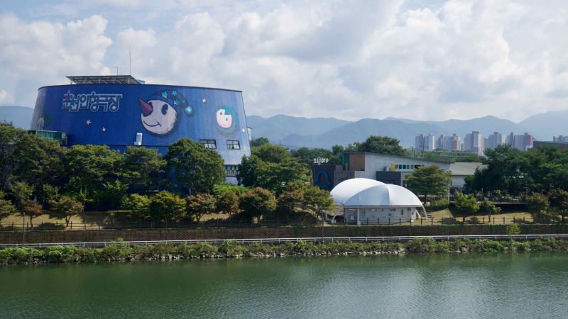 Chuncheon Puppet Theater is viewed across Uiam Lake with hills and apartments beyond.