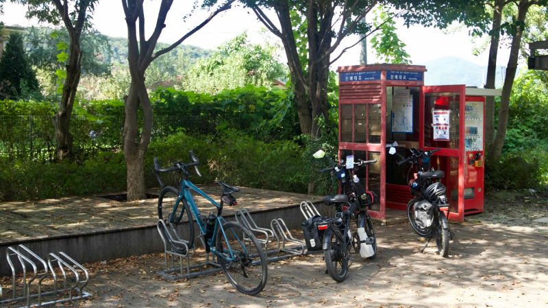 Bicycles are parked next to the red Sinmae Bridge certification booth on the Bukhangang Bike Path.