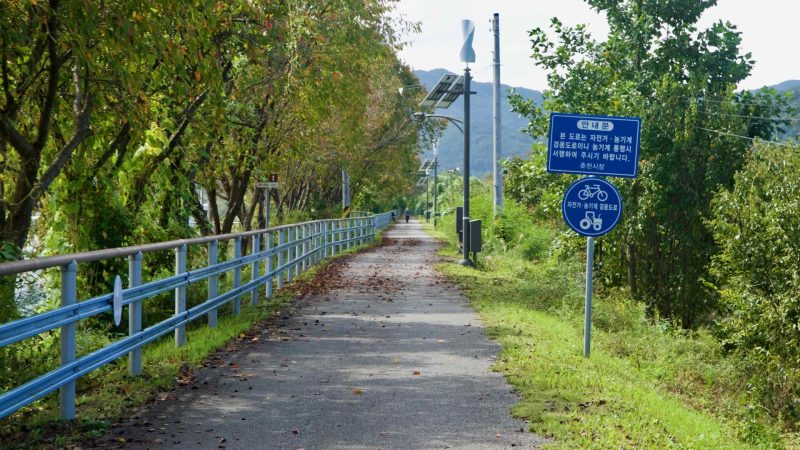 Blue guidance signs mark a shared-use stretch of the bike path near farm fields.