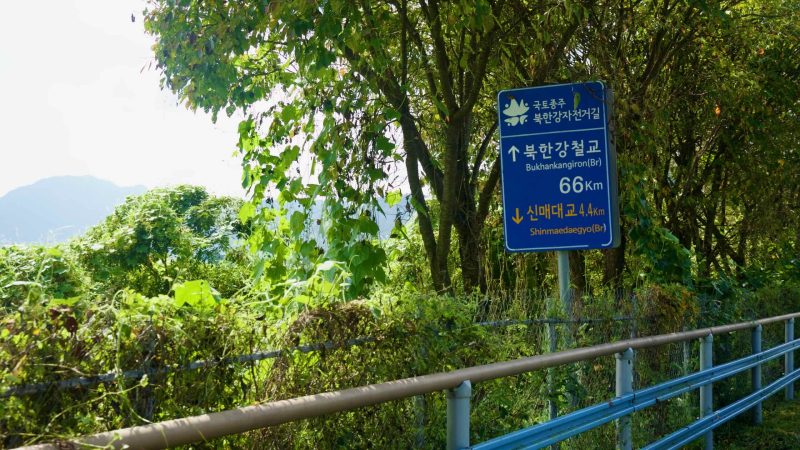 A blue bilingual sign on the Bukhangang Bike Path marks distances to nearby bridges.