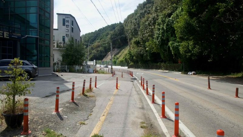 A segregated bike lane threads between orange bollards along Baksa Road on the Bukhangang route.