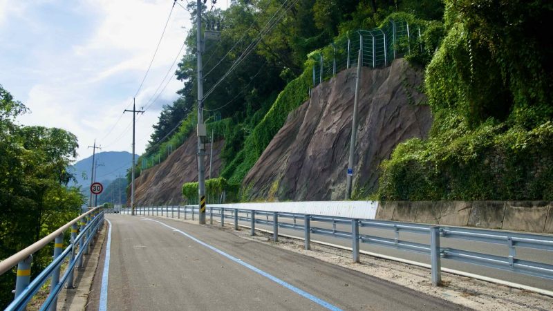 The river bikeway climbs along a cliffside above the Bukhangang in Chuncheon, with the road below.