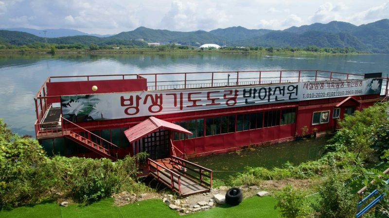 A red floating building with a large Korean banner sits on the river at Uiam Lake.
