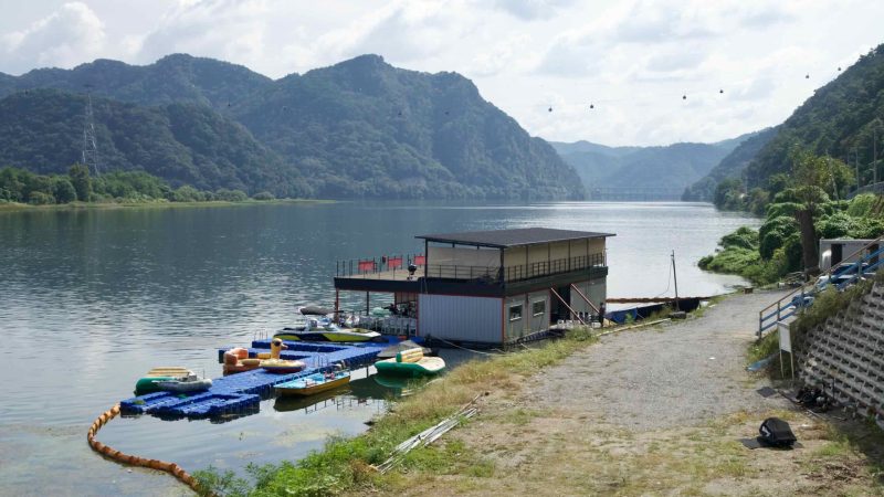 A floating dock and small pontoon building rest on quiet Uiam Lake beneath forested hills.