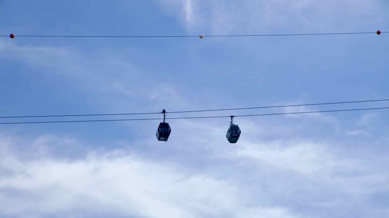 Two gondola cabins ride the Samaksan cable car against a pale blue sky.