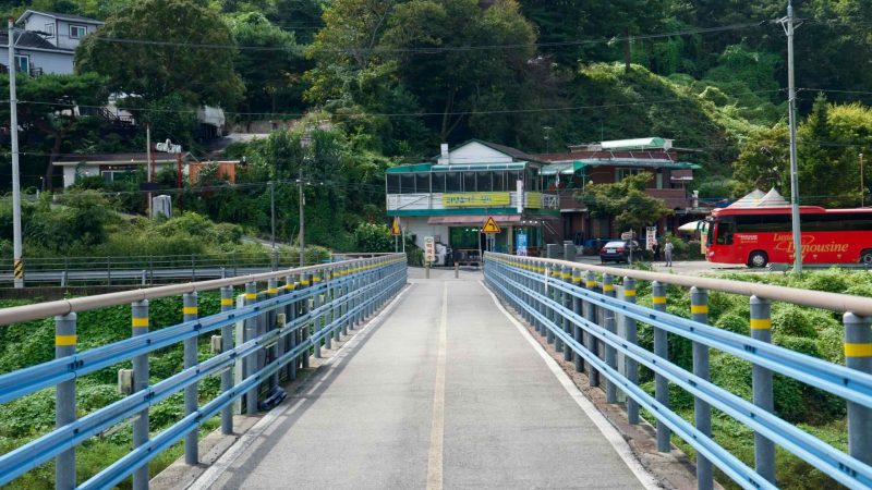 A blue-railed bikeway bridge leads to a small lakeside village on Uiam Lake.