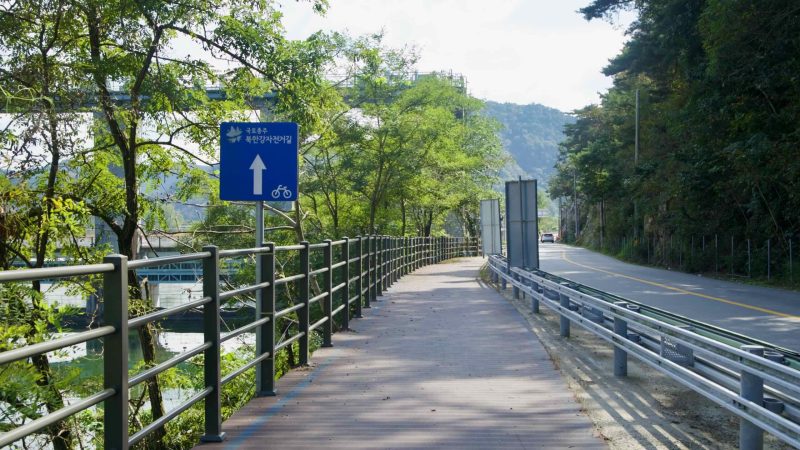 Blue wayfinding signs mark the Bukhangang Bike Path beside the road near Uiam Dam.