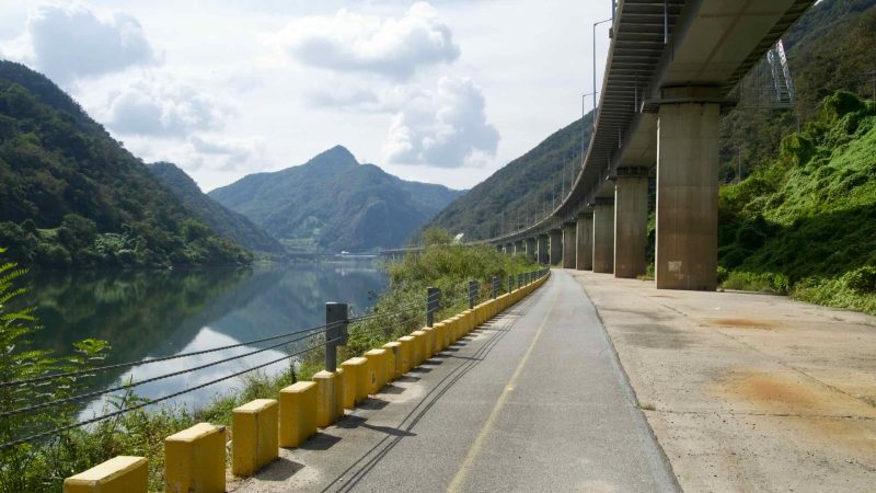 Yellow blocks line the lakeside bikeway under the sweeping viaduct.
