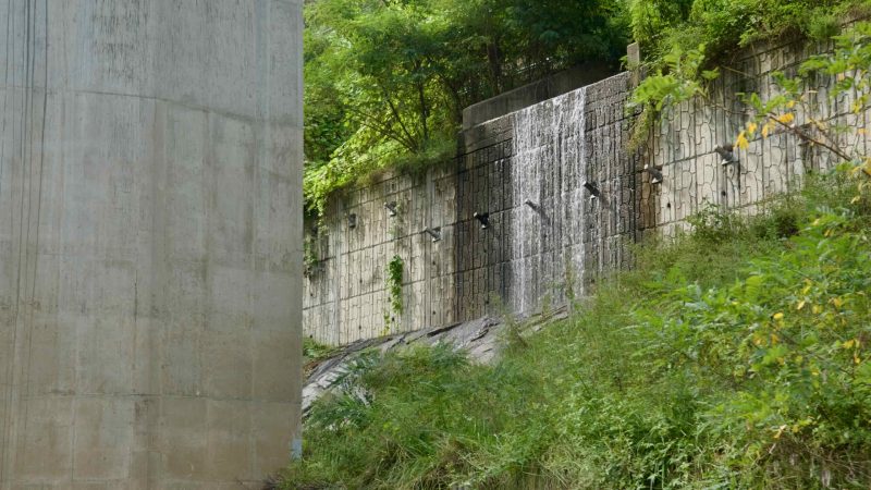 Water cascades across a patterned retaining wall beside the path.