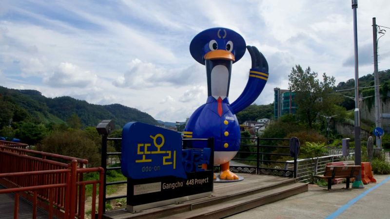 Gangchon’s blue Ddo-ori mascot salutes visitors beside the river walk.