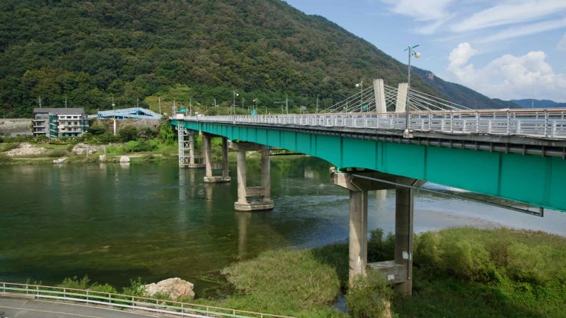 Gangchon Grand Bridge crosses the Bukhangang near Gangchon-ri with green deck and cable-stayed pylons between wooded hills.