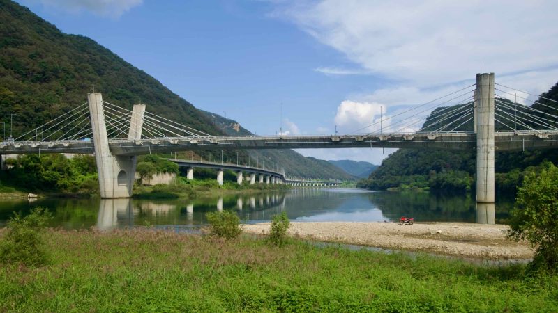 Gangchon Grand Bridge crosses the Bukhangang with cable-stayed pylons, seen from a gravel bar and marshy flats.