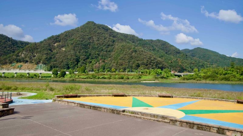 A painted riverside plaza overlooks the Bukhangang and low hills beside Gangchon.