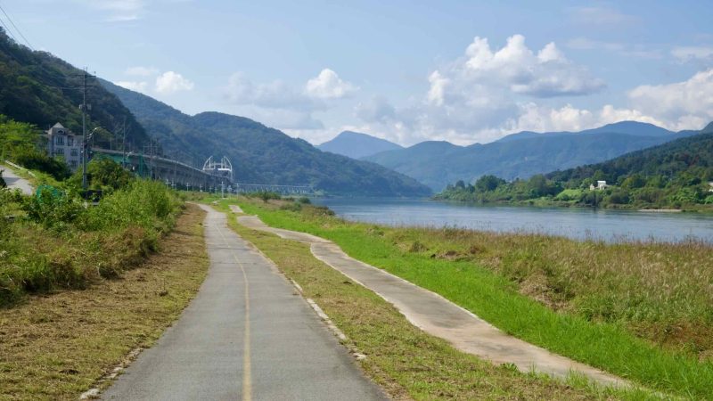 A quiet stretch of riverside path opens views across Lake Uiam and the mountains.