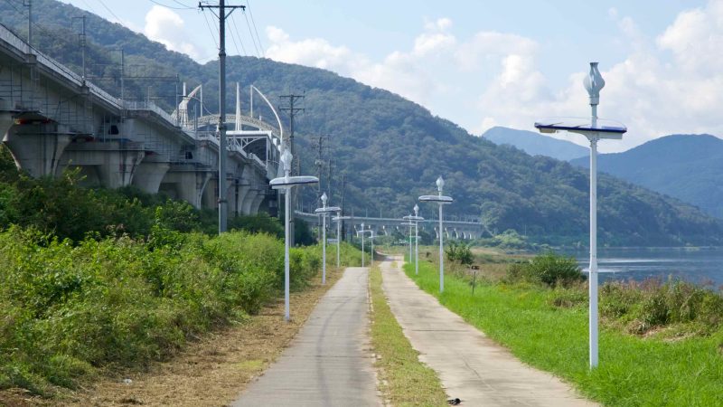 Solar lamps line a riverside walkway beside the bike path and viaduct.