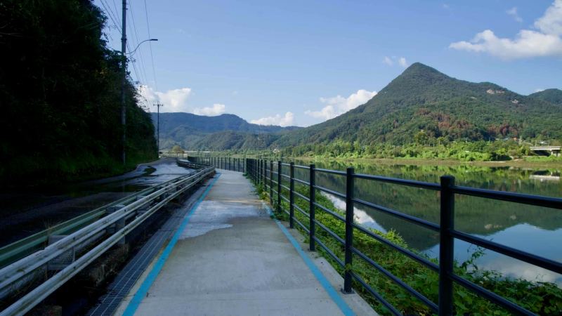 A riverside boardwalk with black railings parallels the calm river.