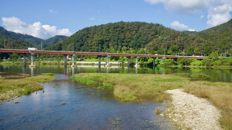 A red-deck road bridge crosses the Bukhangang over shallow gravel bars.