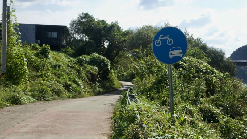 A shared road sign for bicycles and cars stands beside a narrow lane.