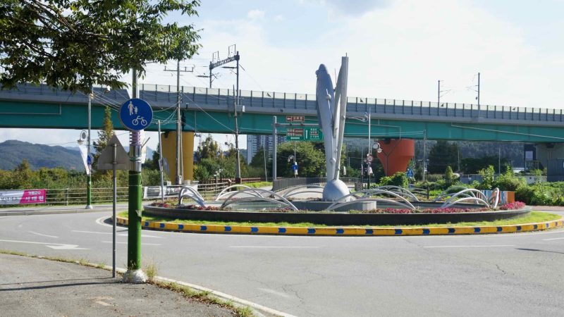 A fish sculpture marks a riverside roundabout below the Gyeongchun Line viaduct in Gapyeong.