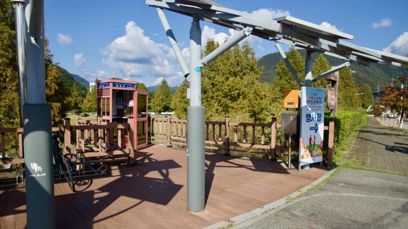 Bike racks stand under a solar canopy beside the Kyunggang Bridge certification booth.