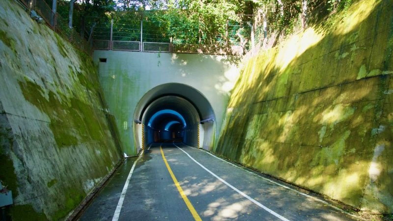 At the opposite portal, blue lighting outlines Saekhyeon Tunnel’s arch as dappled sunlight falls across the path.