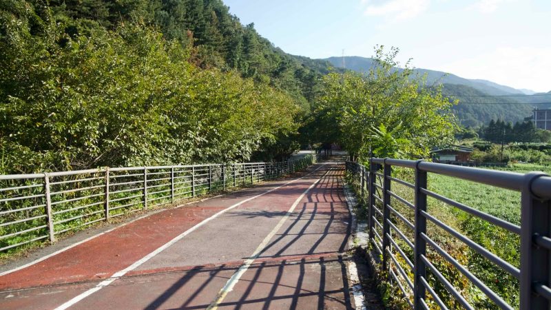 A village bikeway passes homes and a cafe with hills beyond on the Bukhangang route.