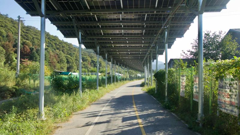 A solar-panel roof on columns casts repeating shadows along the bikeway.