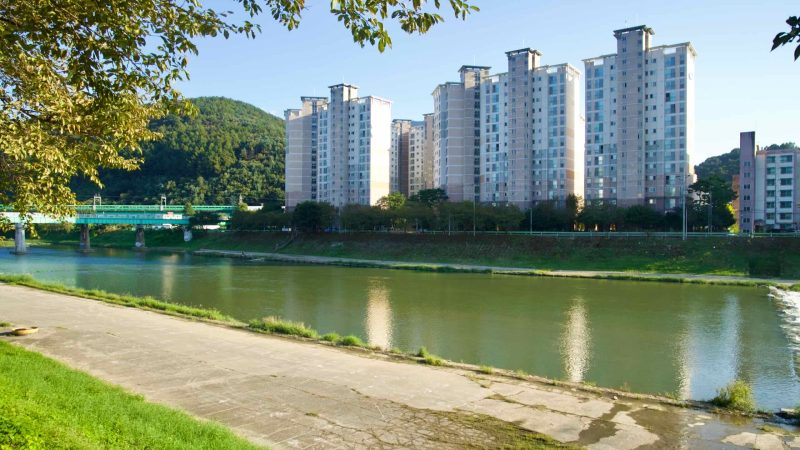 Riverside apartment towers face the Bukhan River at Cheongpyeong as the Gyeongchun Line bridge and a passing train cross nearby.