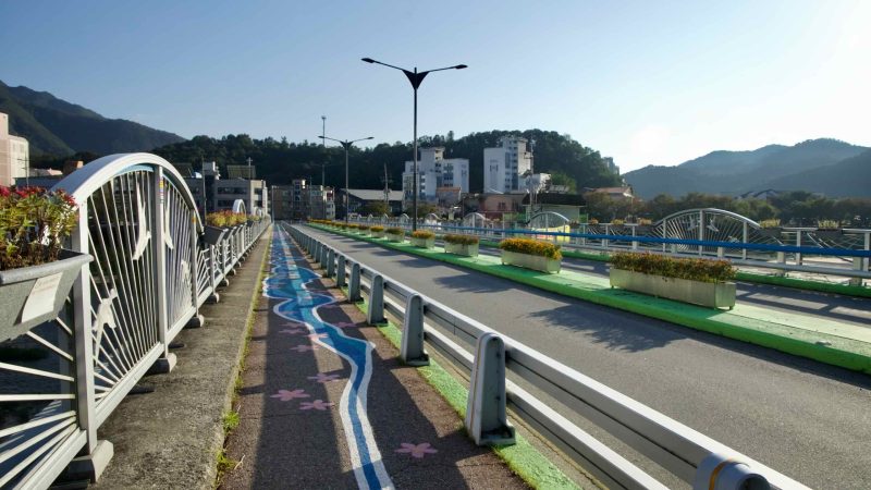 Cheongpyeong Bridge carries traffic past planter boxes and a painted walkway depicting local streams, with low evening light on the hills.