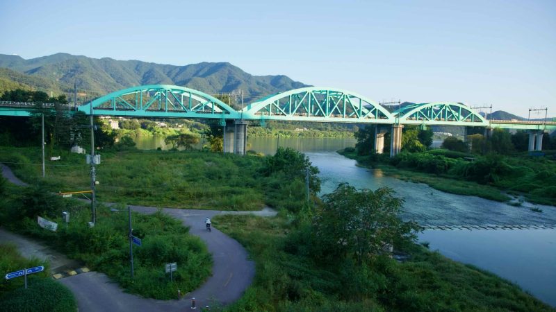 A turquoise truss rail bridge crosses the North Han River near Gapyeong, with the bike path running below.