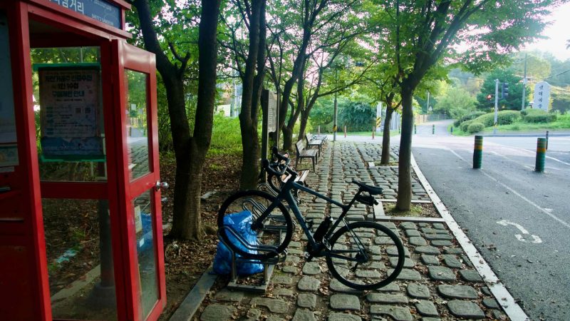 Bike racks stand beside the red Saeteo Samgeori certification booth on the Bukhangang path.