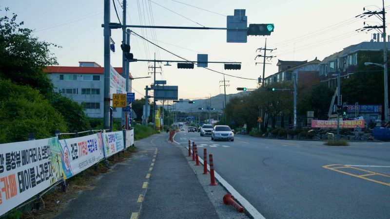 Evening traffic moves under overhead signals along a roadside corridor in Namyangju.