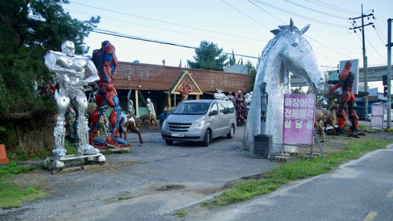 A roadside sculpture yard shows metal robot figures and other artworks in Namyangju.
