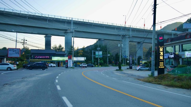 A curving highway and elevated viaduct rise above restaurants and local businesses in Namyangju.