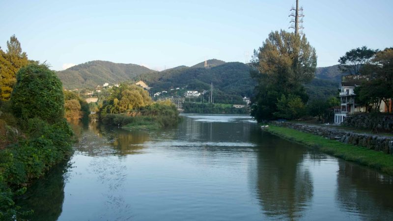 Evening light reflects on the Bukhan River in Namyangju with wooded hills and riverside homes.