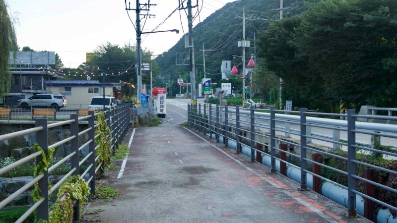 A riverside bikeway crosses a narrow bridge beside a country road in Namyangju.