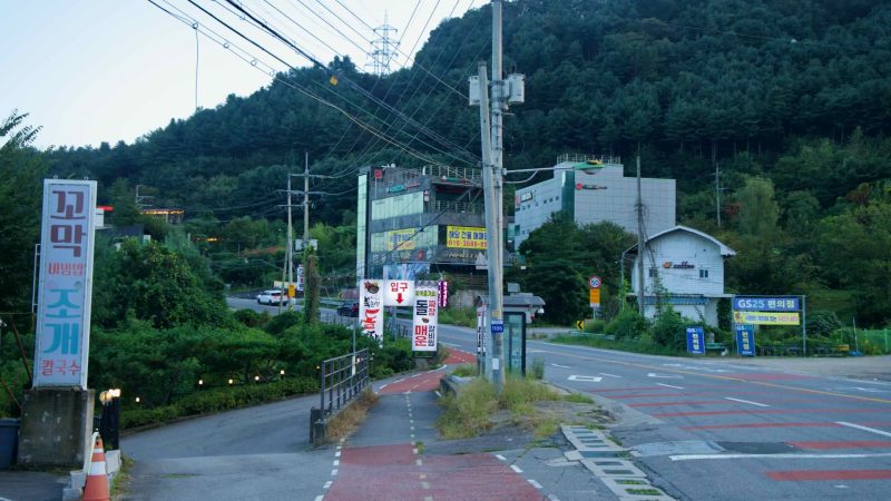 Roadside shops and a red bike lane meet above the river in Namyangju.