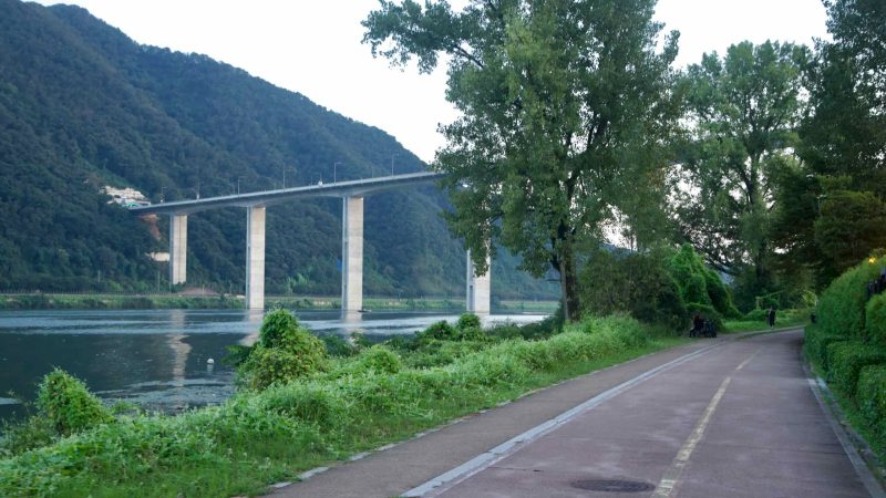 A riverside bike path passes a high viaduct on the Bukhangang in Namyangju.