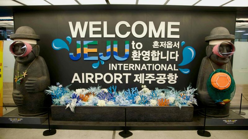 “WELCOME JEJU” sign with dolhareubang statues inside Jeju International Airport.