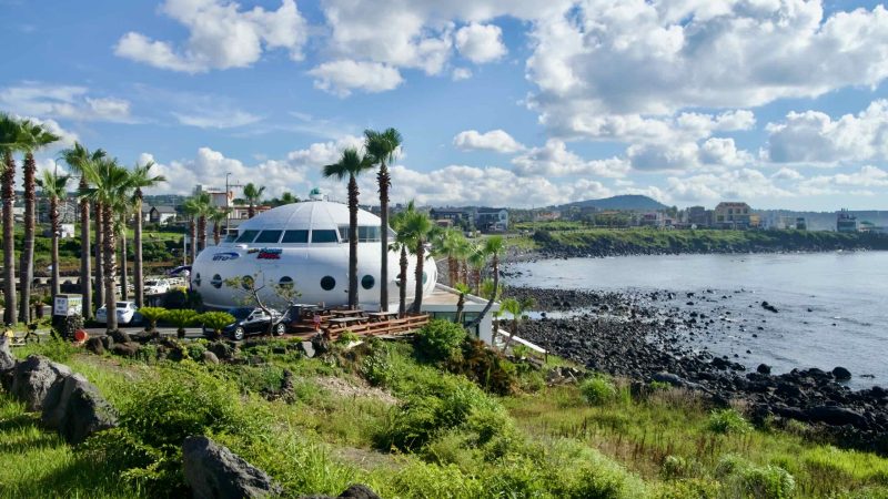 UFO‑shaped café and palms above the rocky Aewol shore on Jeju’s west coast.