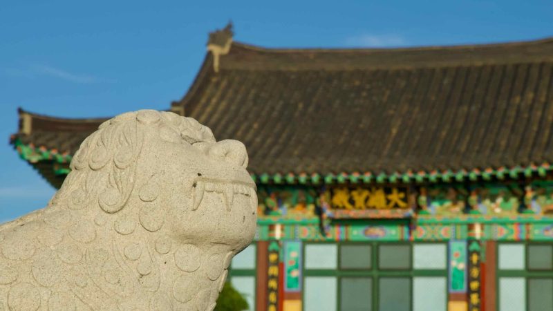 Carved stone guardian lion with Haewoon Temple’s main hall behind.