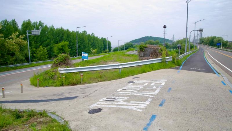 A marked bike path diverges from Jeonho Bridge, leading down toward the Ara Hangang Lock and canal-level facilities along the Gyeongin Ara Waterway.